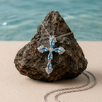 Silver cross necklace with blue stones on a rock by the water