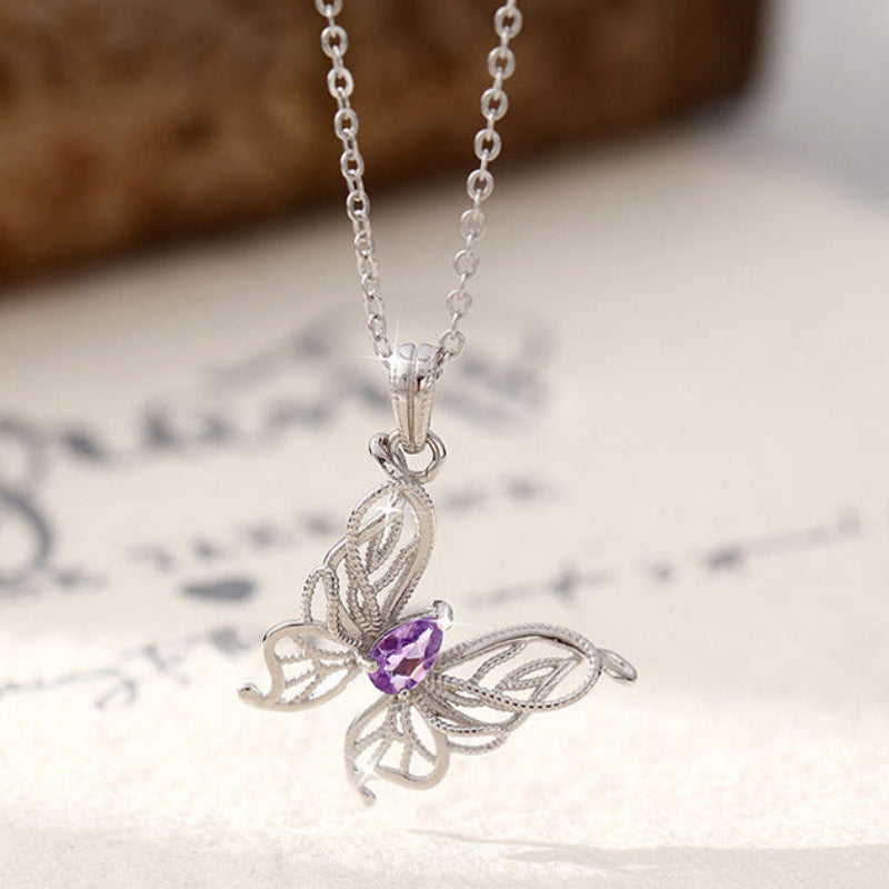 Silver butterfly pendant necklace with a purple gemstone on a textured surface