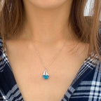 Person wearing a necklace with a sailboat pendant