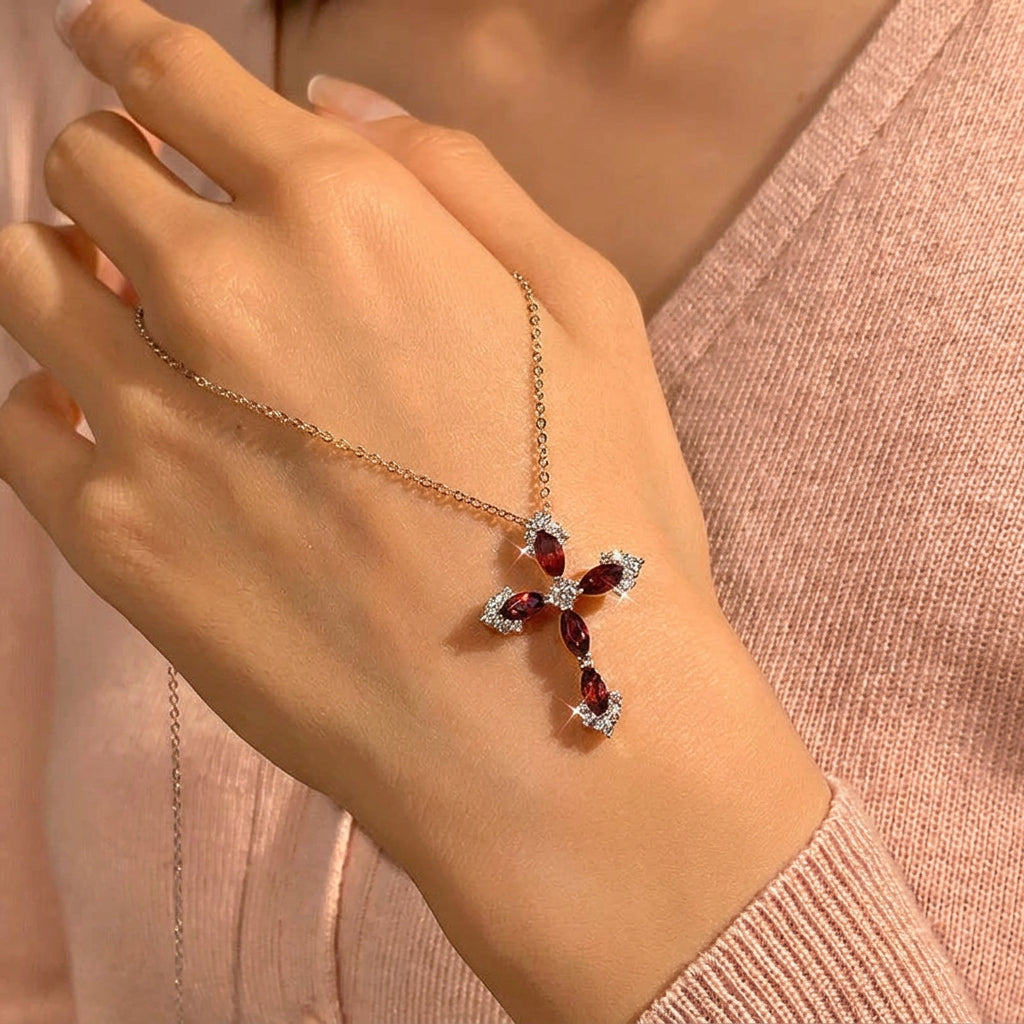Necklace with a cross pendant featuring red gemstones on a hand.