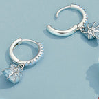 Silver hoop earrings with starfish charms on a light blue background with shells.