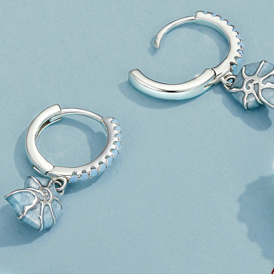 Silver hoop earrings with starfish charms on a light blue background with shells.