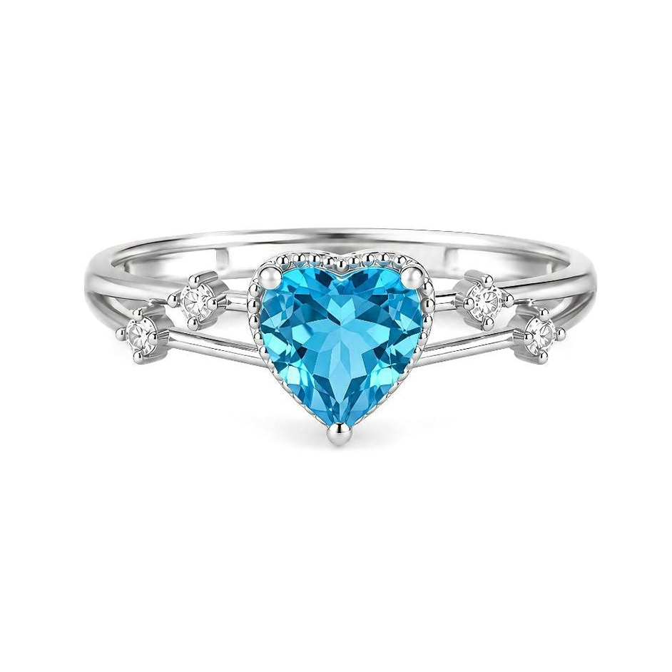 A silver-toned ring shown from multiple angles on a white background. The ring features a heart-shaped light blue gemstone in the center, small clear accent stones, and a split shank with tiny stones.