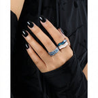 Hand wearing two rings with black nail polish against a neutral background