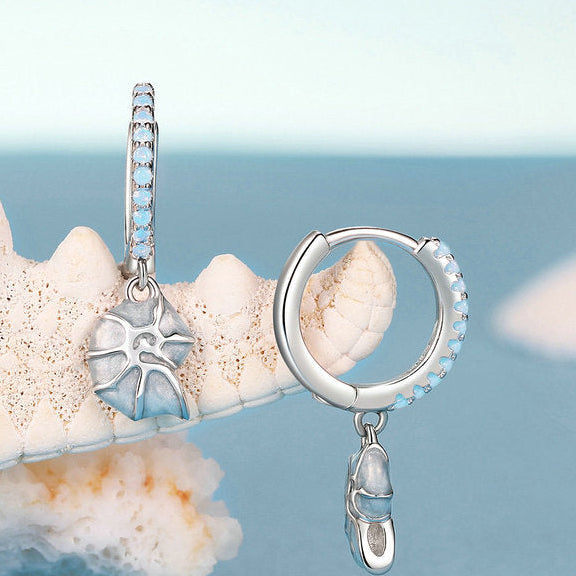 Silver earrings with a starfish charm on a coral background