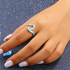 Hand wearing a turquoise wave-shaped ring on a dark glittery background