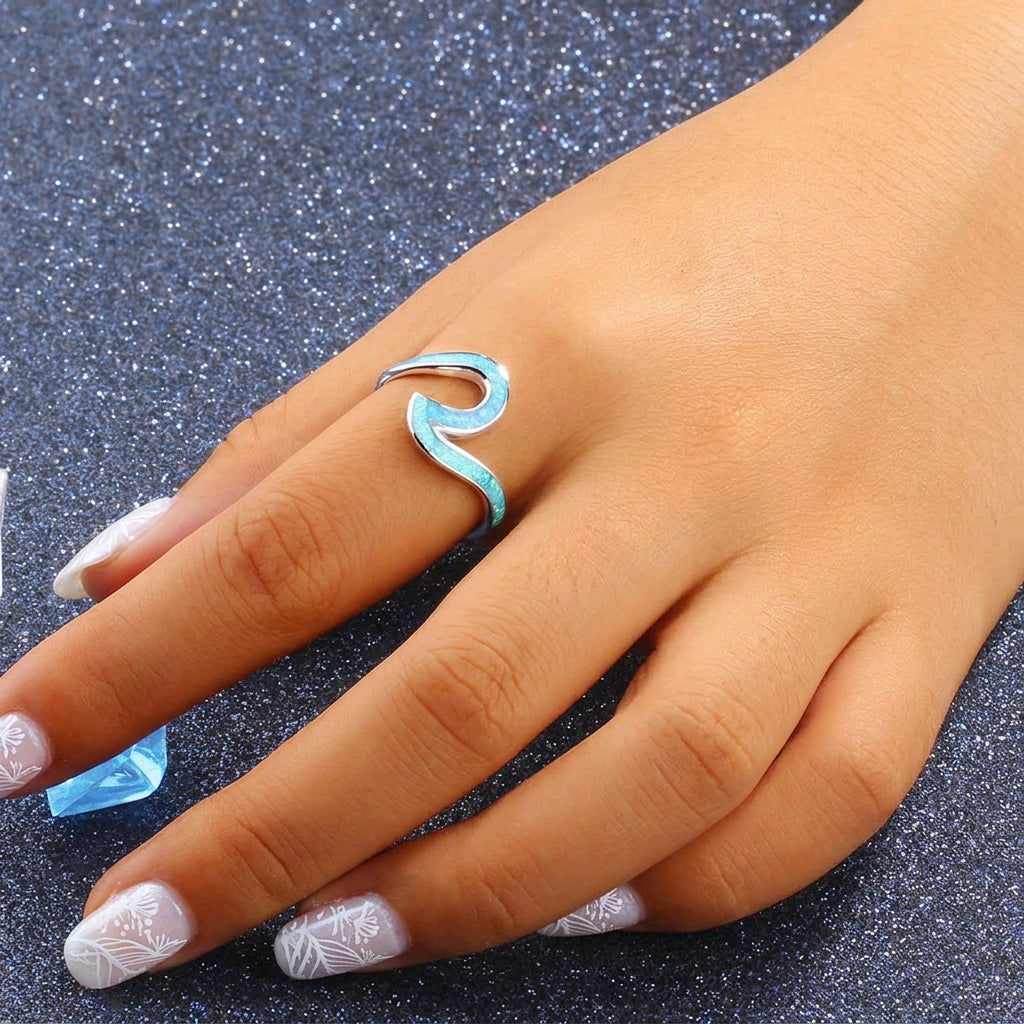 Hand wearing a turquoise wave-shaped ring on a dark glittery background