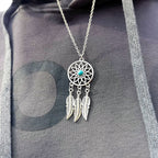 Silver dreamcatcher necklace with feathers and a turquoise stone on a gray fabric background